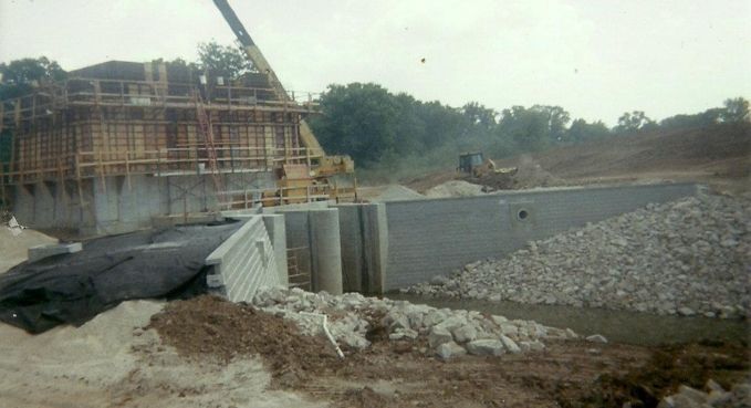 Construction site with a partially built dam and concrete spillway beside a rocky riverbed