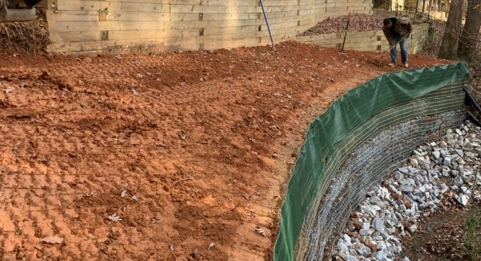 A dirt embankment beside a curved green erosion barrier, with a person standing in the background.