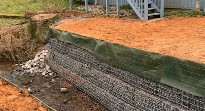 Exposed soil cut beside a retaining wall with green tarp and metal staircase at top