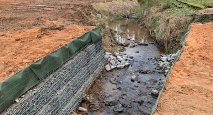 Erosion control barrier lining a narrow creek with rocks and muddy water in a dirt construction area