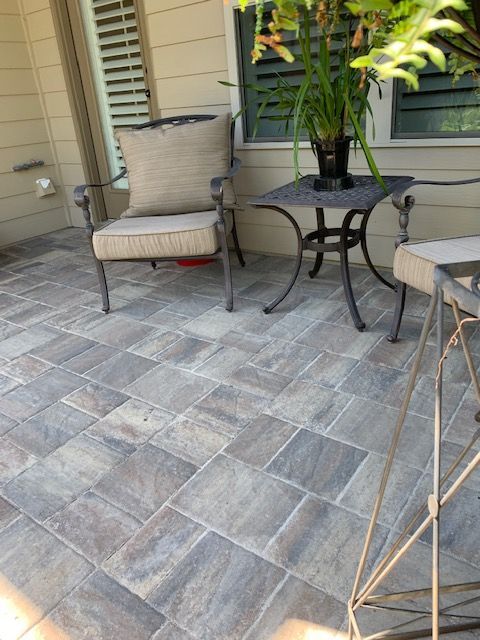 Patio with beige chair, black metal table, potted plant, and gray stone pavers by a house exterior