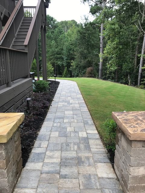 Stone walkway beside a house leading through a green lawn and trees