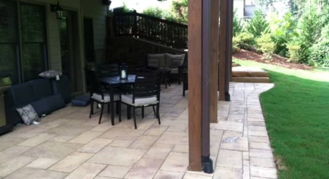 Patio with black outdoor dining set beside a stone walkway and green lawn under a covered overhang