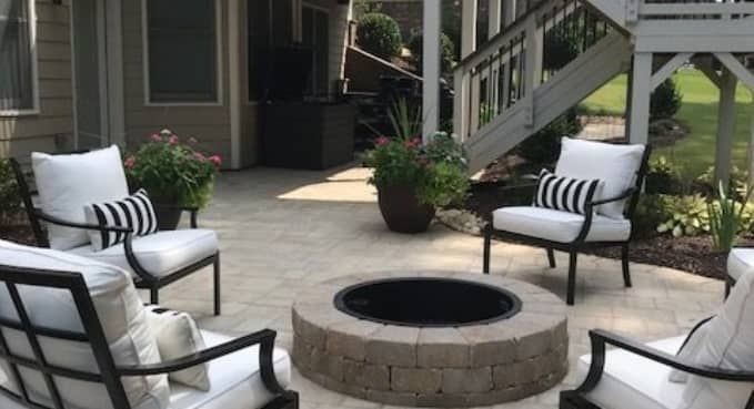 Patio seating area with four striped chairs around a brick fire pit and potted plants on a deck