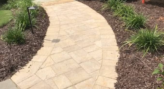 Curved beige stone garden path bordered by mulch and green plants