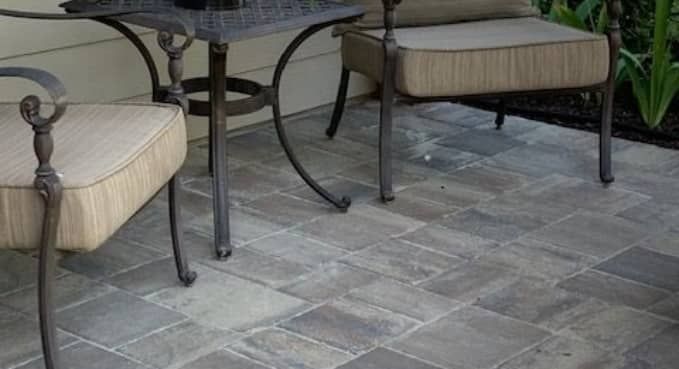 Two beige patio chairs beside a dark metal table on a gray stone patio