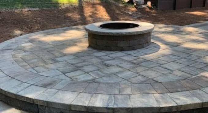 Circular stone patio with a central fire pit in a wooded outdoor area