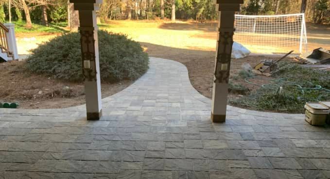 Stone patio path leading to a grassy yard with trees, shrubs, and a soccer goal in warm sunlight