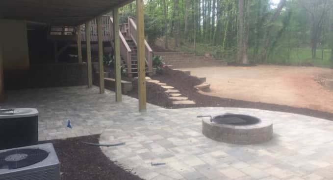 Covered patio with stone pavers, fire pit, stairs, and wooded yard beyond