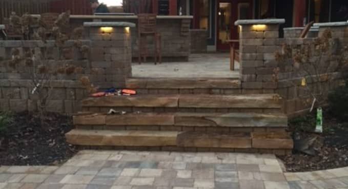 Stone front steps leading to a brick house entrance, with brick retaining walls and patio pavers.