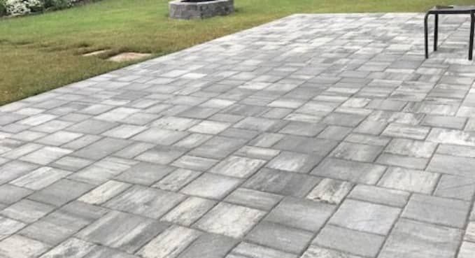 Gray stone-paver patio beside a grassy lawn, with a small table at the edge.