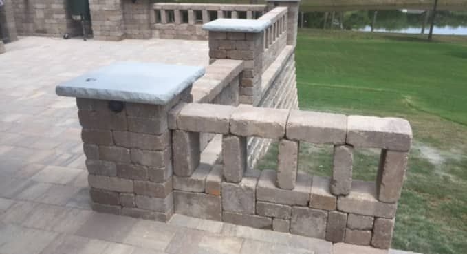 Brick patio wall with stone caps and decorative openings beside a grassy lawn