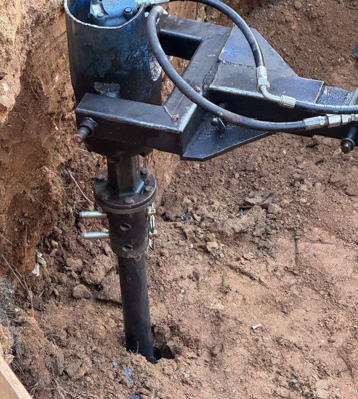 A hydraulic auger drilling a narrow hole in brown dirt.