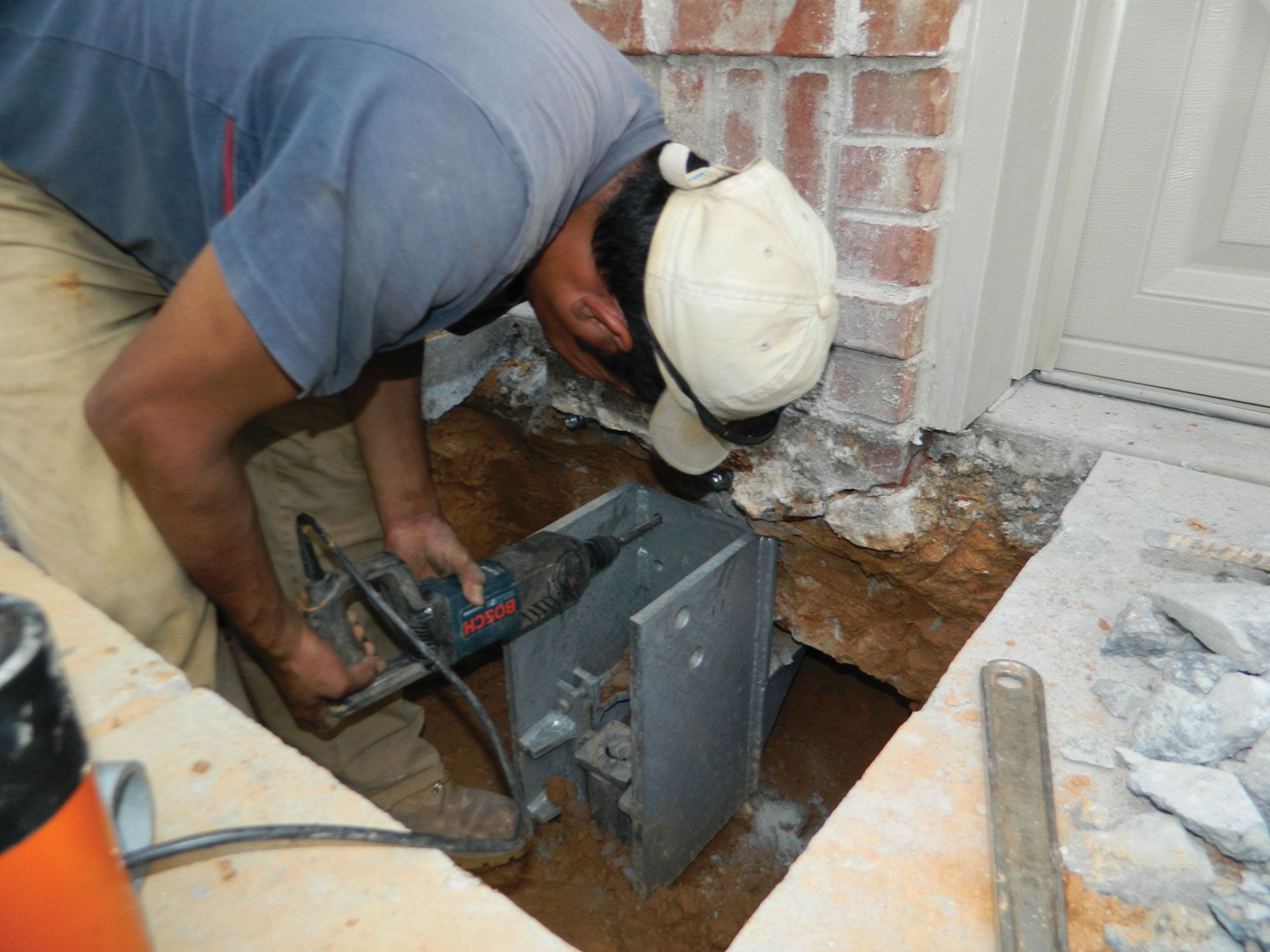 Worker using a drill to cut through concrete near a brick wall and door frame