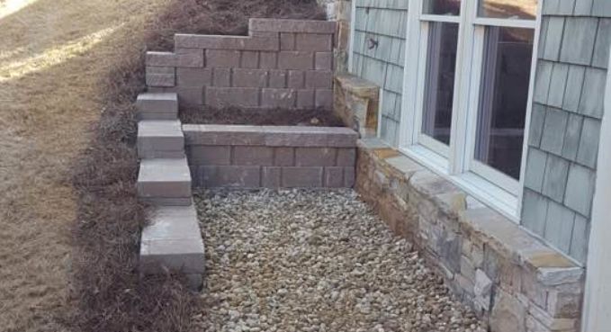 Stone steps and retaining walls beside a house, leading up a narrow gravel path.