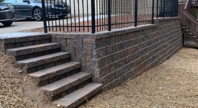 Stone steps beside a brick retaining wall leading to a fenced patio area with parked cars in the background