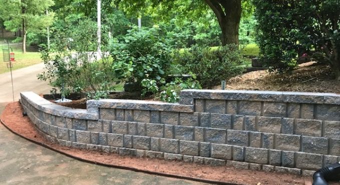 Curved gray stone retaining wall along a garden path with trees and shrubs