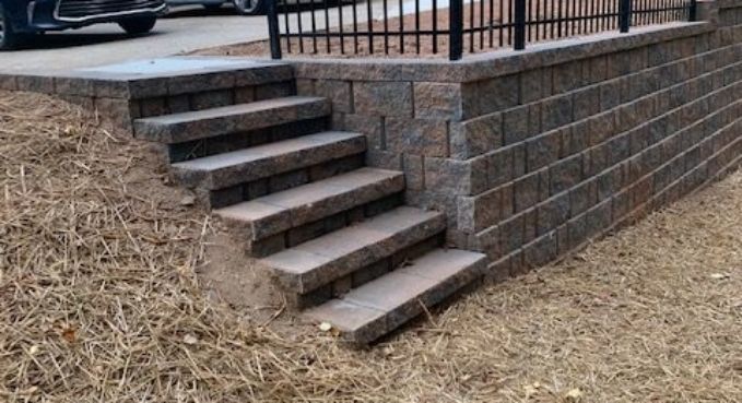 Outdoor brick steps beside a retaining wall and black railing, next to a pile of mulch or straw.