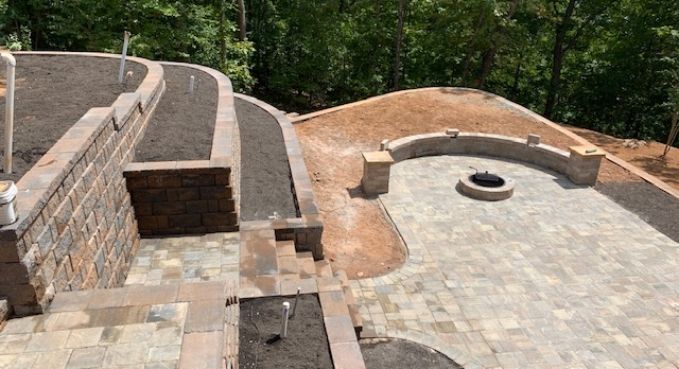 Stone patio and curved retaining walls around a circular fire pit, with wooded hillside beyond.