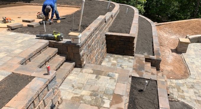 Stone patio under construction with curved retaining walls and a worker laying pavers