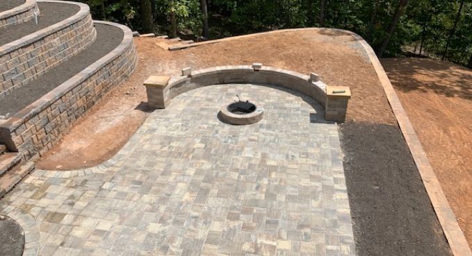 Stone patio with a curved built-in seating area and fire pit in a landscaped yard