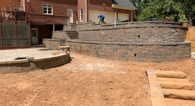 Terraced stone retaining walls in a backyard under construction beside a brick house