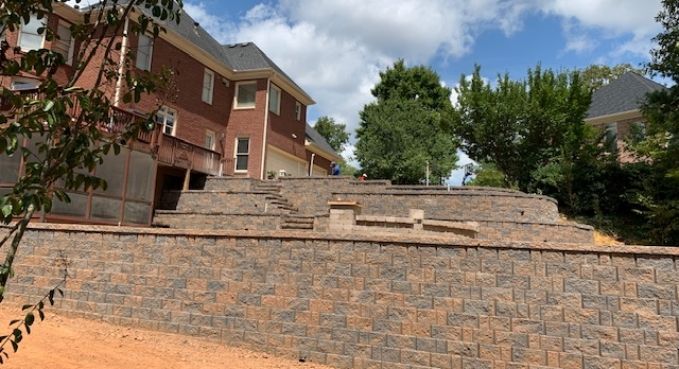 Brick retaining wall and apartment buildings on a sunny hillside under a partly cloudy sky