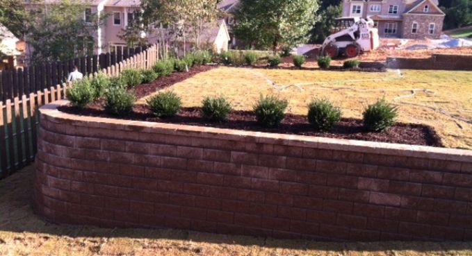 Brick retaining wall with shrubs and a landscaped yard behind it