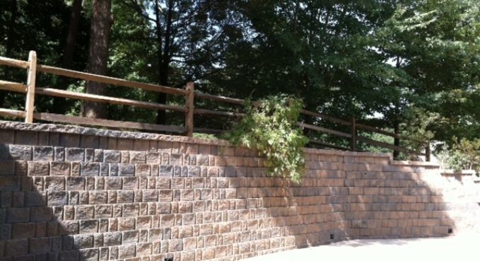 Stone retaining wall with wooden fence and leafy trees above in sunlight