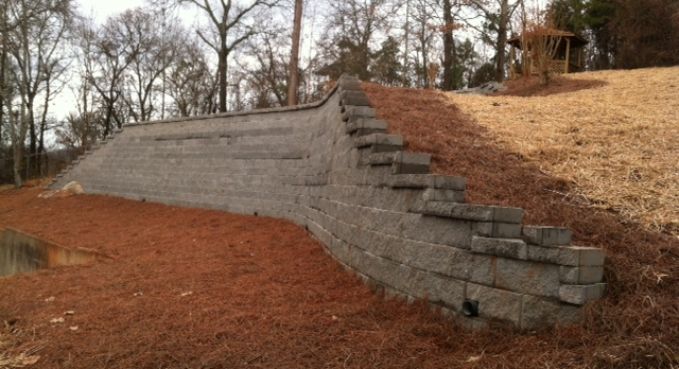 Terraced stone retaining wall along a sloped, leaf-covered hillside with bare trees in the background