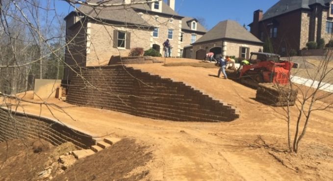 Terraced dirt retaining wall construction beside a suburban house, with excavators and bare trees