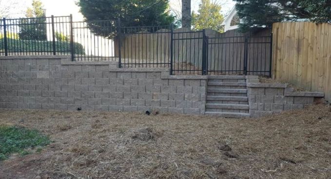 Stone retaining wall with black metal fence and steps leading to a raised yard.