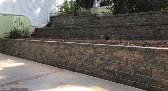 Stone retaining wall and concrete walkway beside a house, with steps leading up a landscaped slope