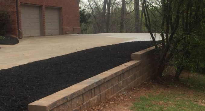 Driveway with fresh black mulch beside a brick retaining wall and garage in a suburban yard
