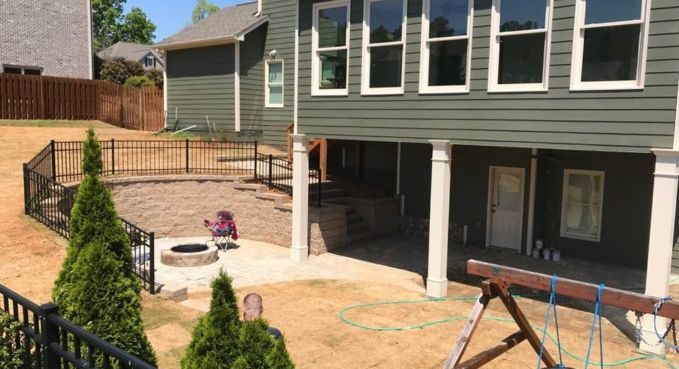 Backyard patio with stone pavers, white columns, and green house exterior in sunlight