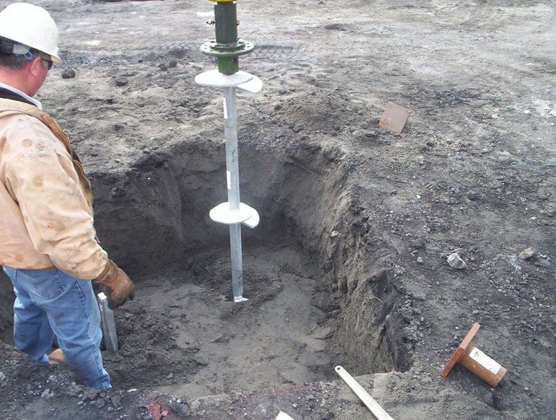 Worker in hard hat using a post-hole auger at an excavation site