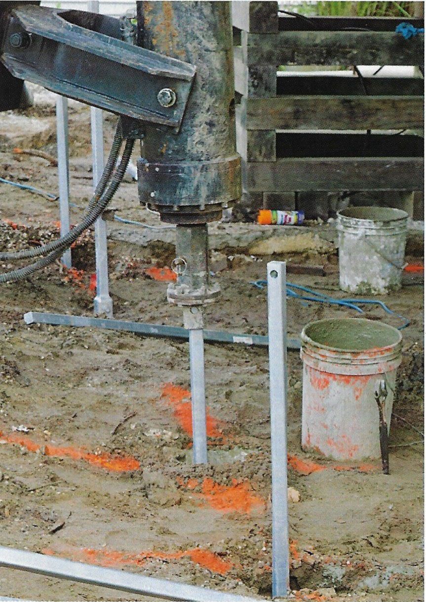 Drilling rig boring into muddy ground beside white PVC pipes and buckets on a construction site