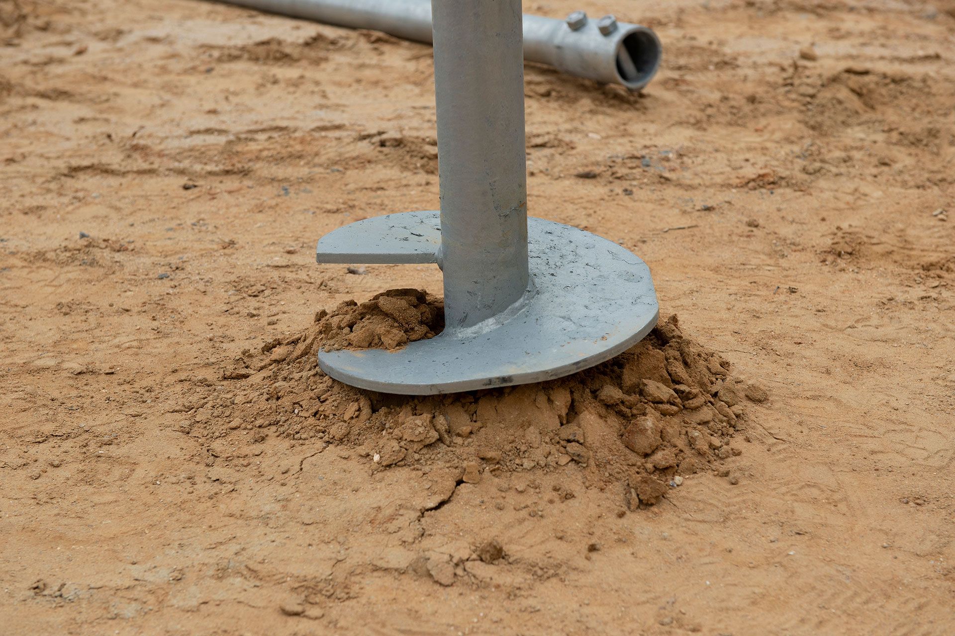 Close-up of a metal ground anchor with a rounded base embedded in sandy soil.