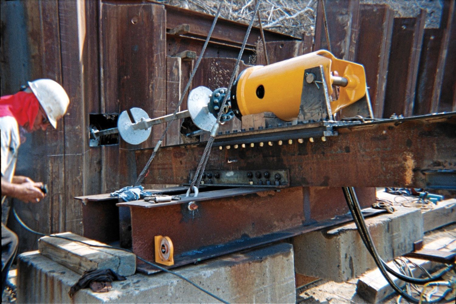 Worker operating a metal-cutting saw on a rusty beam in an outdoor yard