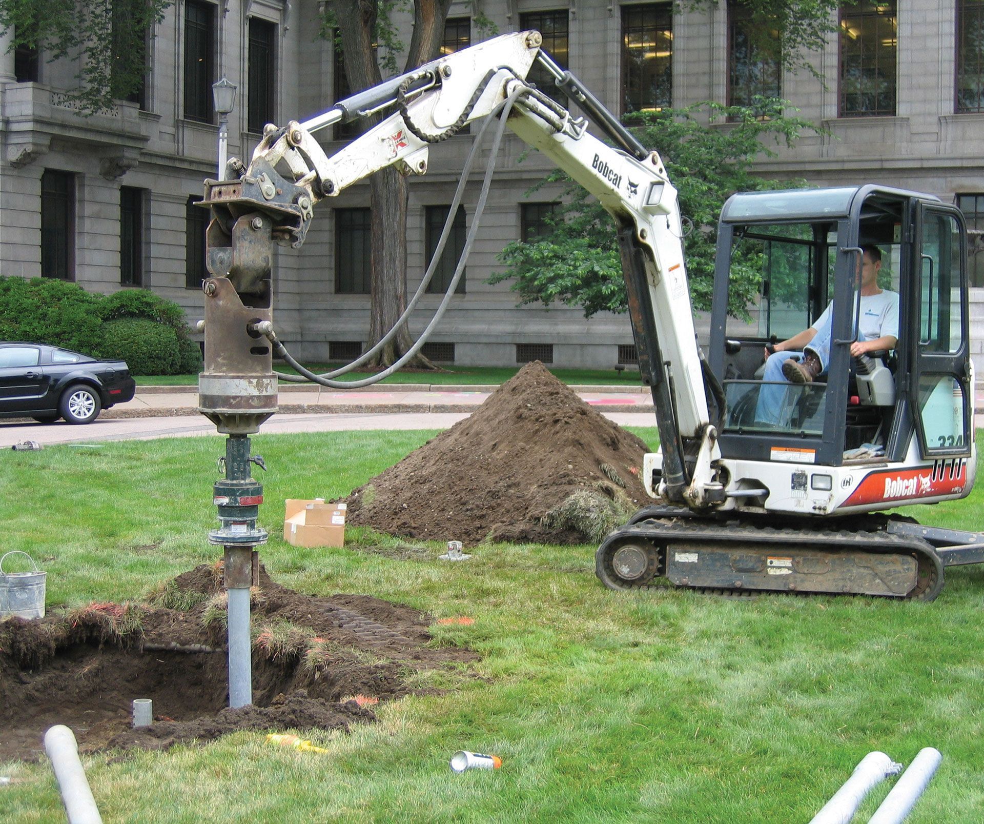 Excavator drilling a hole beside a building on a grassy construction site
