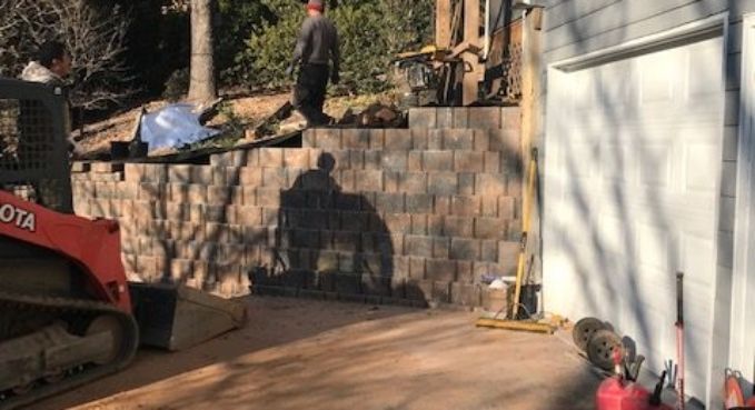 Construction equipment beside a stone retaining wall and white garage door in a driveway