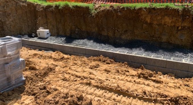 Graded construction site with exposed soil, concrete retaining wall, and stacked pallets on the left