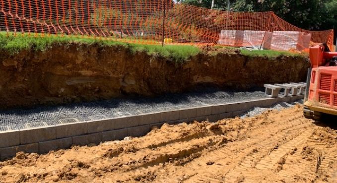 Construction site with trench, orange safety netting, dirt embankment, and excavator on sandy ground