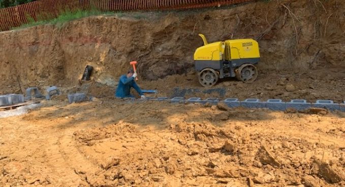 Construction worker beside yellow cement mixer on an earthen roadside site