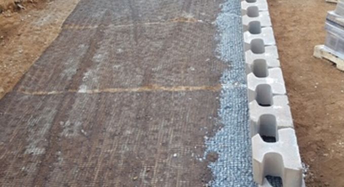 Construction site with gravel drainage strip beside a wooden form and concrete blocks along the edge