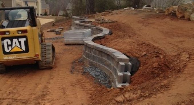 CAT construction vehicle beside curved stacked concrete retaining wall on a dirt road construction site