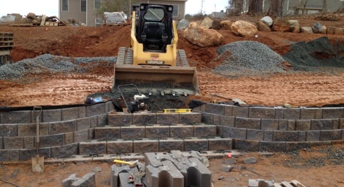 Yellow bulldozer on a muddy construction site, leveling dirt behind stacked retaining blocks.