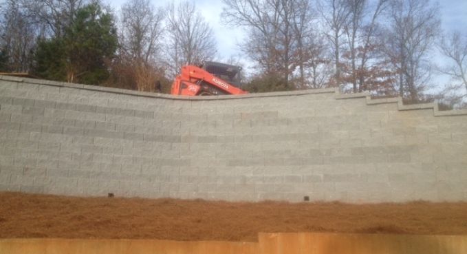 Orange excavator behind a curved concrete retaining wall at a construction site
