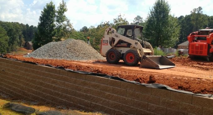 Skid steer loader moving dirt on a construction site, with gravel pile and red machine nearby