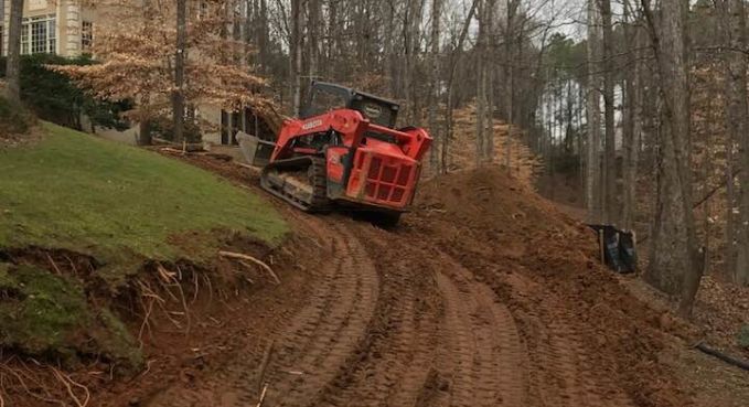 Red tracked utility machine climbing a muddy dirt slope in a wooded hillside area